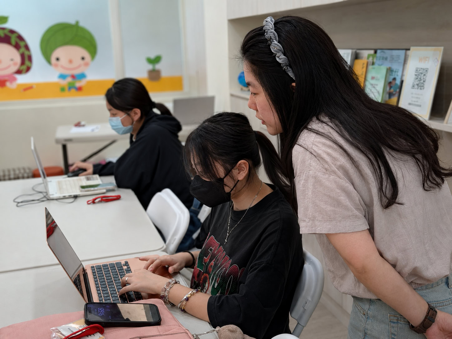 Ning, seated in the foreground, working on a laptop during an e-commerce course while an instructor offers guidance