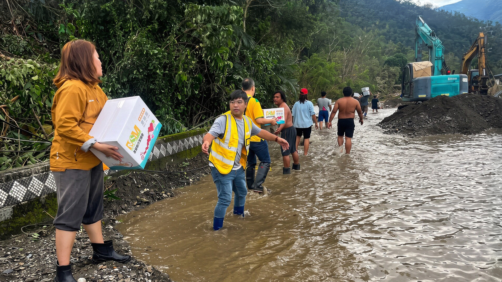 MSM relief workers and community members carrying emergency supplies through floodwater in a mountain community