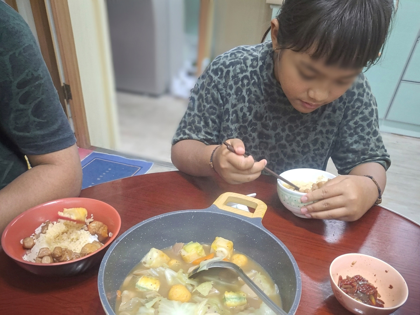 Shan sharing a Warm Meal Box dinner with her family at home; her face is blurred for privacy