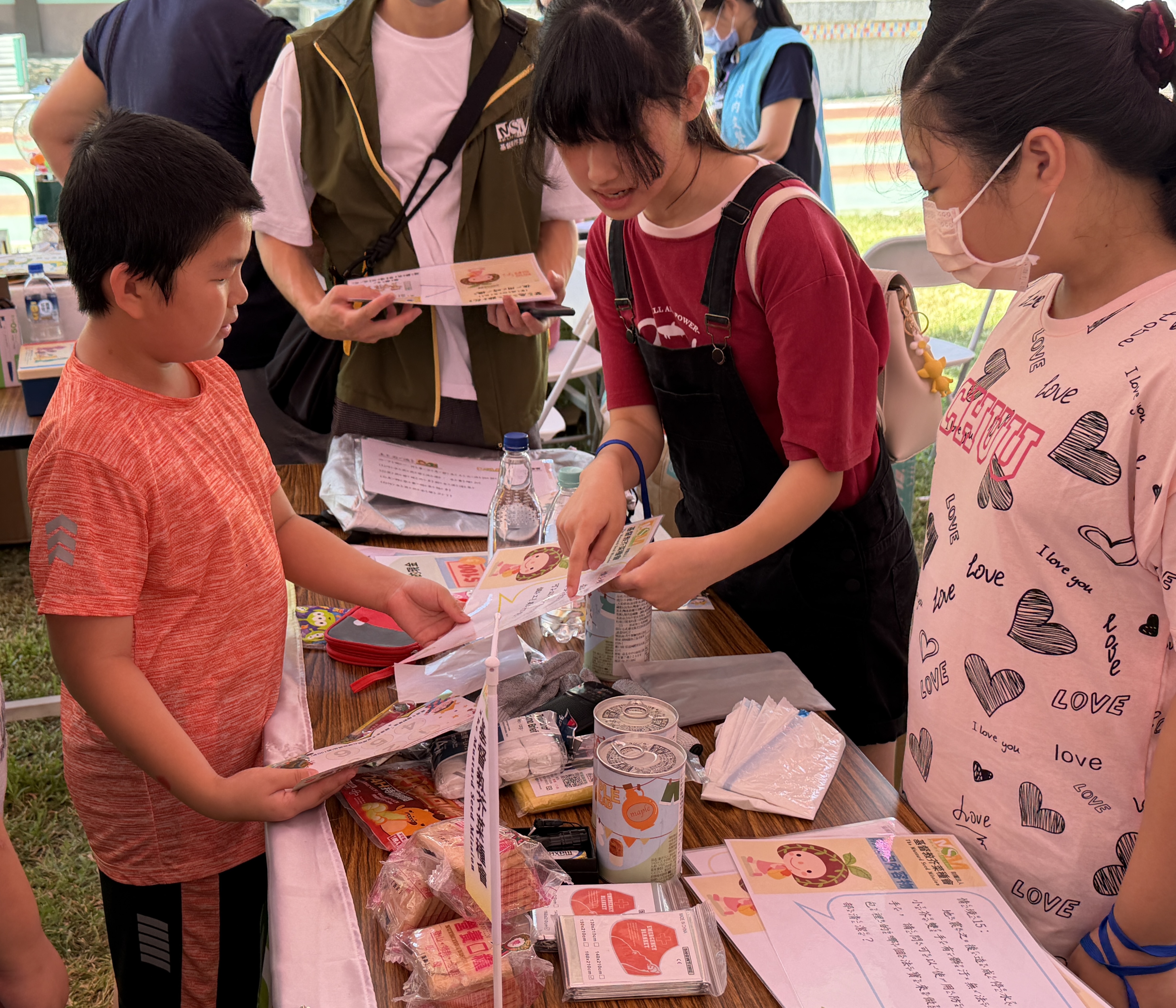 孩子們（右）化身防災小老師，介紹防災包內容，有罐頭、口糧、保暖毯及雨衣等。